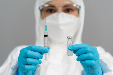 doctor in PPE suit holding vaccine bottle and syringe injection medicine