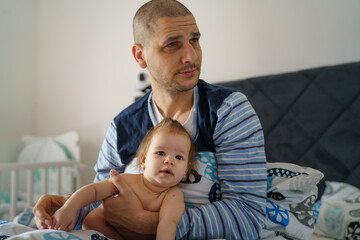 Baby and father adult caucasian man hold his six months old daughter girl on the bed wearing blue pajamas in the morning at home parenthood family domestic life bonding concept real people copy space