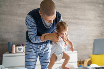Baby and father adult caucasian man hold his six months old daughter girl on the bed wearing blue pajamas in the morning at home parenthood family domestic life bonding concept real people copy space