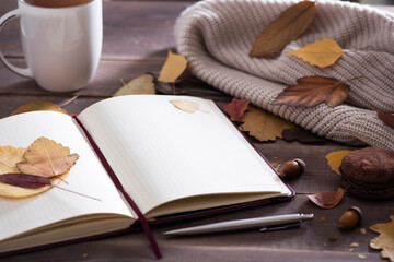 Autumn season concept, beautiful autumn composition with notebook, tea сup, autumn leaves, chocolate macoroon on rustic wooden table, natural background.