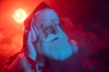 Santa claus listens to music with headphones at a party. Blue red neon light and smoke.