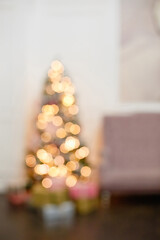 Blurry interior with a Christmas tree. Christmas and New Year's bright interior in focus. Lots of glowing lights . Background with bokeh. Vertical frame