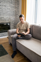 A young man is using a digital tablet. A guy is typing while sitting on a sofa