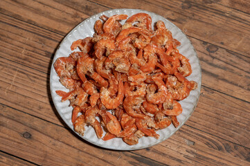 Shelled fresh shrimps on a plate or bowl are on a wood colored table