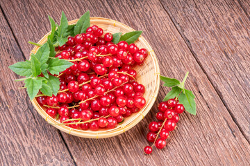 Red currant in bamboo basket on wooden background, Red currant berries with leaf on wooden table.