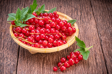 Red currant in bamboo basket on wooden background, Red currant berries with leaf on wooden table.