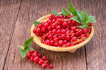 Red currant in bamboo basket on wooden background, Red currant berries with leaf on wooden table.