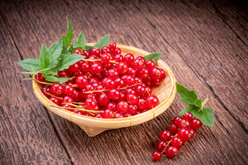 Red currant in bamboo basket on wooden background, Red currant berries with leaf on wooden table.