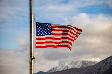 United States of America flag flying half mast with blue sky, clouds and mountain background in the north during fall, autumn season. 