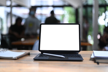 Computer tablet with blank display, stylus pen and notebooks on office desk.