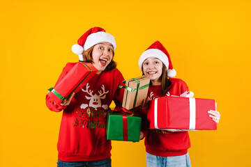 Portrait of Latin sisters girls holding Christmas gift box on a yellow background in Mexico latin...