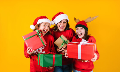 Portrait of Latin mother and daughters holding Christmas gift box on a yellow background in Mexico latin America