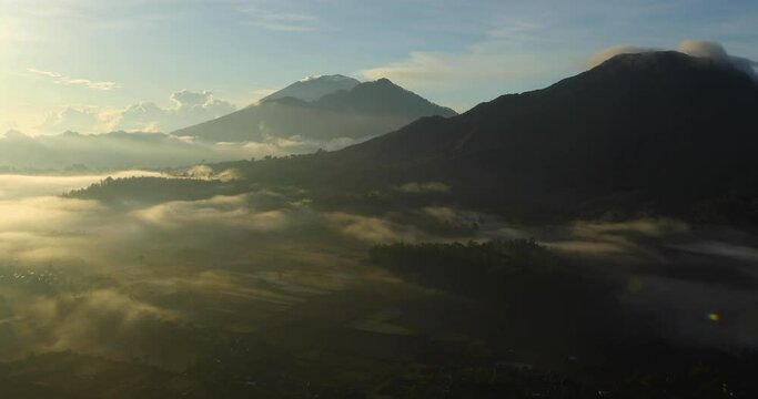 Sunrise panorama in the Kintamani region of Bali in Indonesia with the volcanoes Batur, Abang and Agung slowly awakening in the mist.
