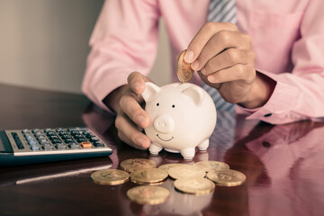 The hand of a businessman puts coins in a piggy bank, saves money with coins, steps into a...