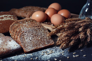 Fresh loaves of bread with wheat and gluten on a black table. Bakery and grocery concept. Fresh, healthy sorts of rye and white loaves food closeup. Fresh homemade bread with cereals.