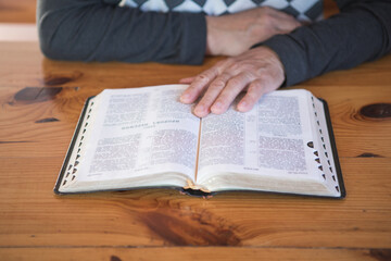 Naklejka premium senior man praying, reading an old Bible. Hands folded in prayer on a Holy Bible in church concept for faith, spirituality and religion