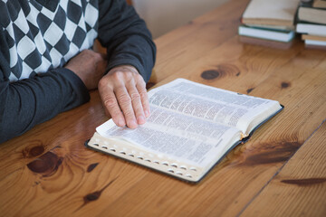 senior man praying, reading an old Bible. Hands folded in prayer on a Holy Bible in church concept for faith, spirituality and religion