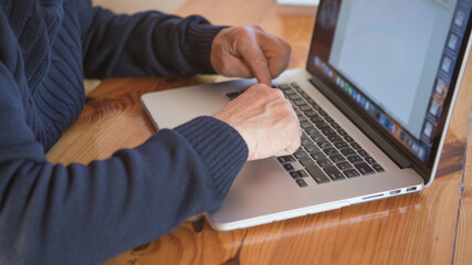 Old hands on the keyboard. Retired person  learn to use computer. Old man working on laptop at home. Senior man using computer in living room, sitting on chair and looking at screen. Elderly grandfath