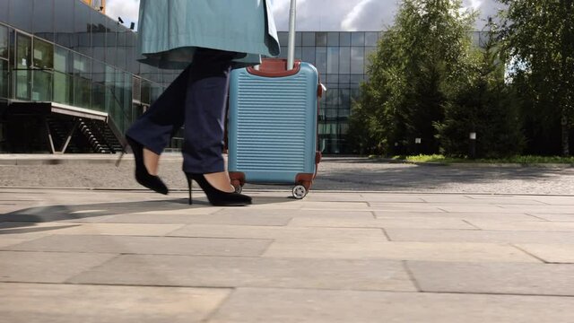 Closeup of young woman traveler moving suitcase and walking along airport building on autumn spbi. View of legs of successful businesswoman holds luggage in hand and walks outdoors on background of