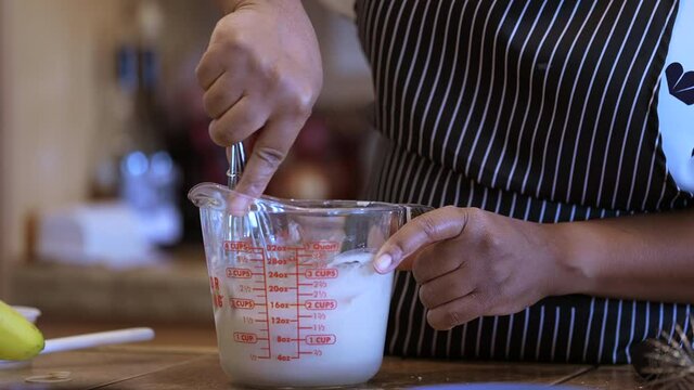 Stirring icing in a measuring cup with a metal whisk - side view in slow motion
