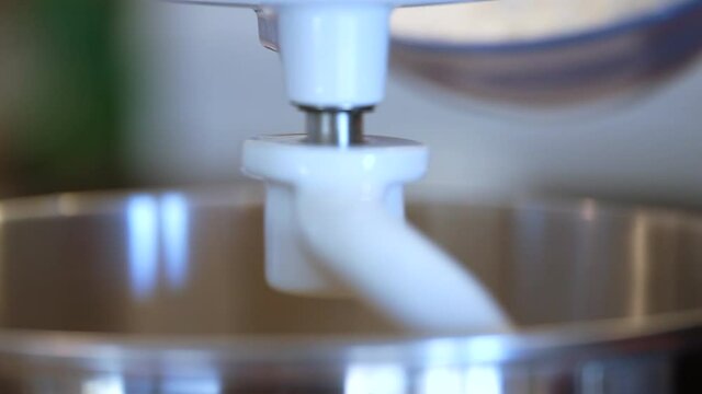 Adding flour to the wet ingredients on a professional mixer and dough hook - side view close up in slow motion