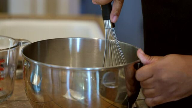 Hand mixing a homemade recipe in a stainless steel bowl with a whisk in slow motion