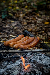 Man hand turns frying grill sausages on fire. Selective focus, visible smoke