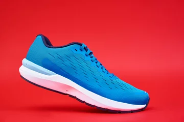 Gordijnen Blue running sneaker on red background, close up © Lazy_Bear