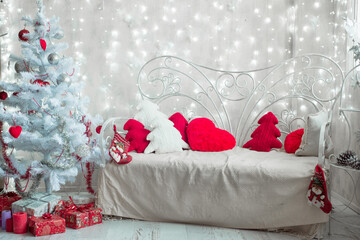 Decorative Christmas pillows on the bed. Pine tree shape knitted white and red pillows on sofa with lights