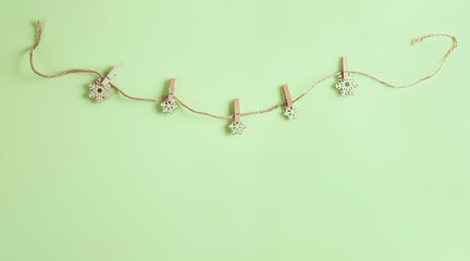 Five handmade wooden snowflakes on the rope with the pegs on the green background and place for your text. Christmas or New Year beige and green banner.