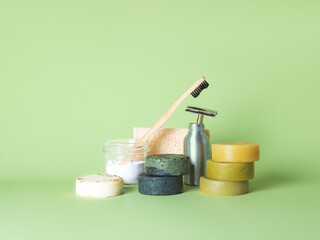 The bamboo toothbrush in the glass with toothpowder and the steel multiple-use razor, six natural round soaps and the natural wash gourd against the green background. Zero waste bathing concept.
