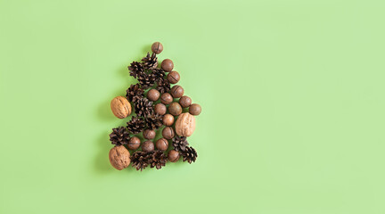Christmas or New Year natural composition of nuts and cones in the form of the fir tree on the green background. Beige and green greeting card for your design, banner.