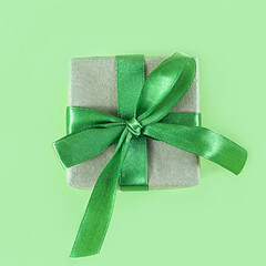 The above view on the present packed in the craft paper with the green satin ribbon on the green background. Minimalism New Year or Christmas concept.