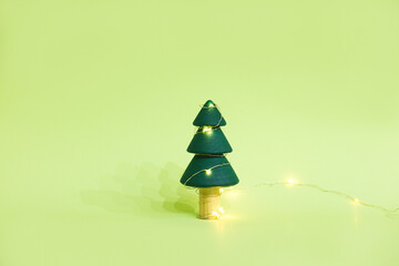 The wooden handmade fir tree with the twinkle lights on it on the green background. Christmas or New Year concept for your design.