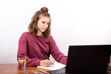 Teenage schoolgirl writes notes watching video online webinar study on laptop sitting at table distance e-learning course videoconference call from pc white background