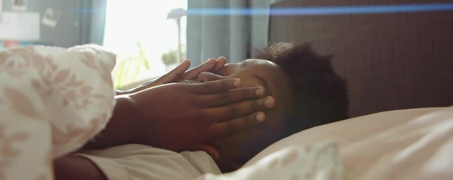 Close up shot of young sleepy African American woman lying in bed and rubbing her eyes and face after waking up in morning