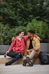 Happy young man with Down syndrome and mentoring friend sitting with arms around outdoors
