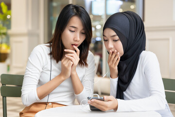 two asian woman friends watching the same streaming suspense, horror movie show or receiving bad news and being surprised together