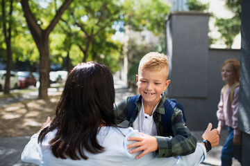 Happy schoolboy running to his grandmother waiting for him after school outdoors in street.