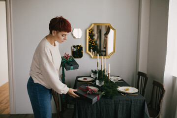 Young woman serving Christmas table with beautiful festive tableware. Preparations for holiday dinner.