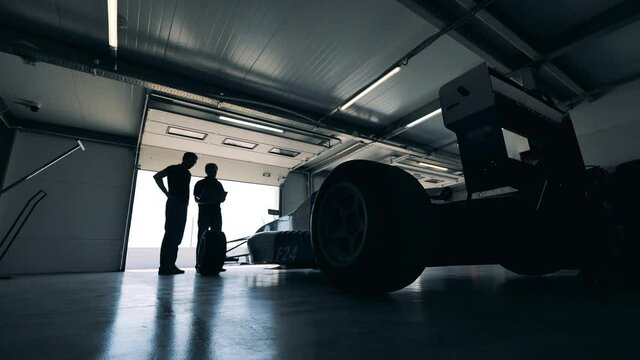 Sports car is being observed by two racers in a garage