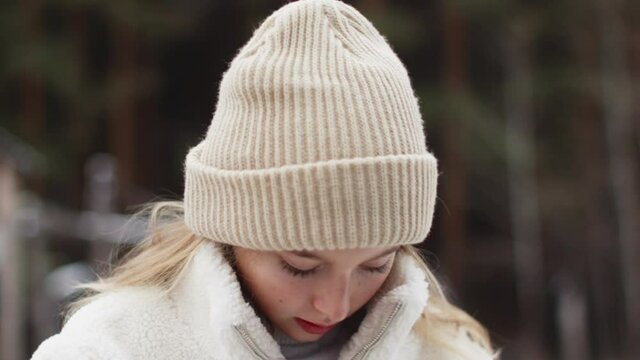 Portrait beautiful teenager white girl zip up fur jacket on winter street. Young woman in knitted hat zipping up winter jacket outdoor.