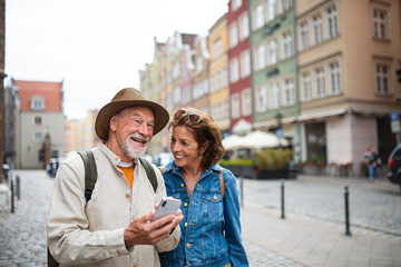 Portrait of happy senior couple tourists using smartphone outdoors in historic town