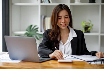 Shot of an Asian young businesswoman working on a laptop computer in her workstation.Portrait of Business people employee freelance online marketing e-commerce telemarketing concept.