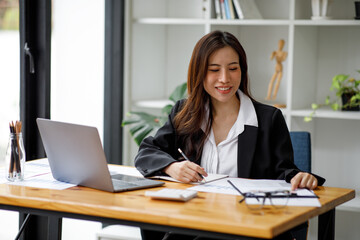 Shot of an Asian young businesswoman working on a laptop computer in her workstation.Portrait of Business people employee freelance online marketing e-commerce telemarketing concept.