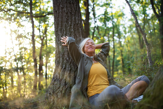 Portrait of senior woman relaxing and sitting with eyes closed outdoors in forest.