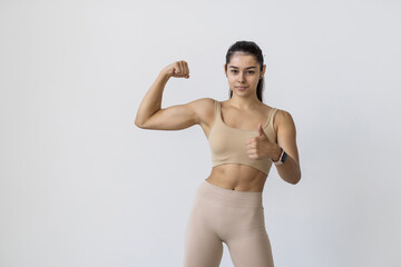 Beautiful young woman show biceps with thumbs up on white background. Strength and motivation. - obrazy, fototapety, plakaty