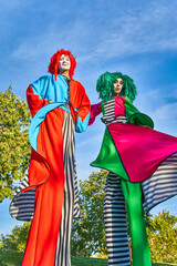 Positive stilt walkers in multicolored costumes standing together in park