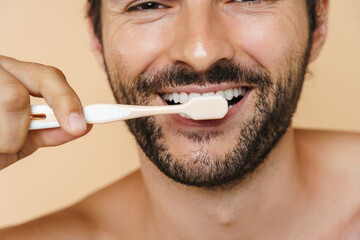 Naklejka premium Young half-naked man smiling while brushing his teeth