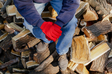 Man in jeans sits on top of pile of firewood